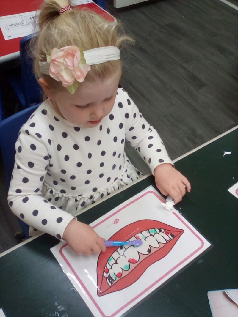 A child colouring in a teeth brushing activity sheet at a table