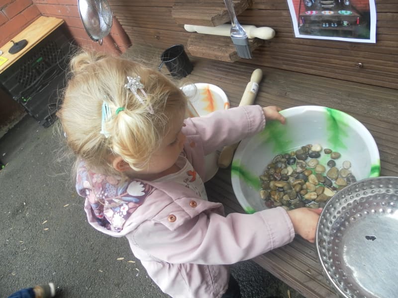 A child mixing leaves and water in a bowl at the mud kitchen