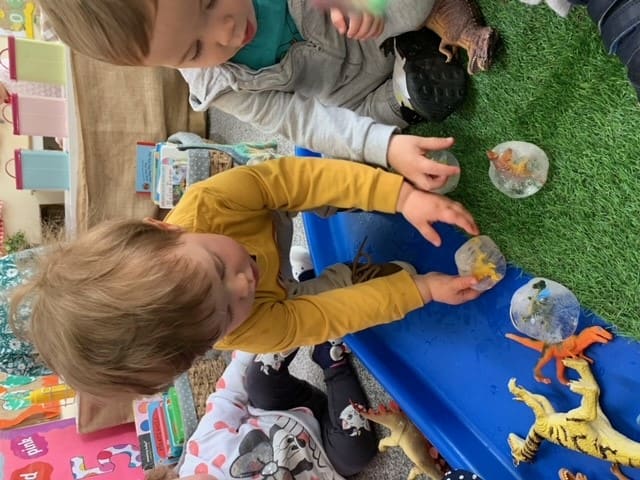 Children playing with dinosaurs and small world toys at a tray